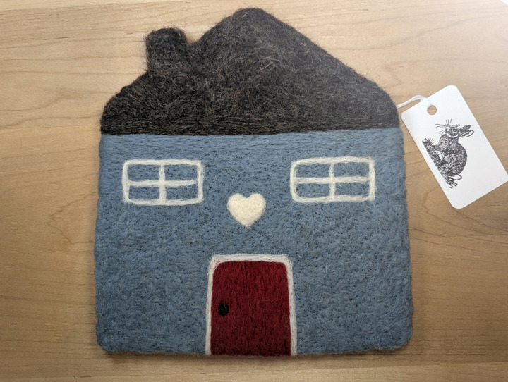 A felted country blue house with a brown roof and a red door with a white heart motif above it.