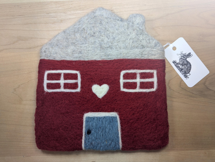 A felted red house with a light grey roof and a country blue door with a white heart motif above it.
