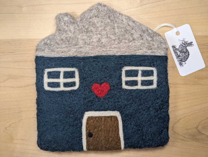A felted hunter green house with a light grey roof and a brown door with a heart motif above it.