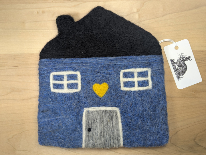 A felted heather blue house with a black roof and a grey door with a yellow heart motif above it.