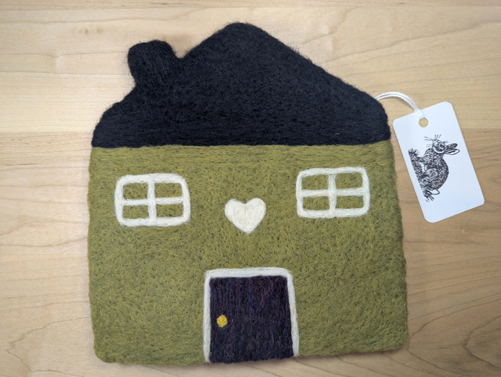 A felted olive green house with a black roof and mulberry door with a white heart motif above it.