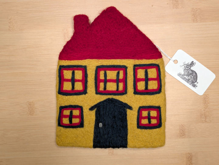 A felted yellow house with a red roof, green and red trim around the windows, and a green door.