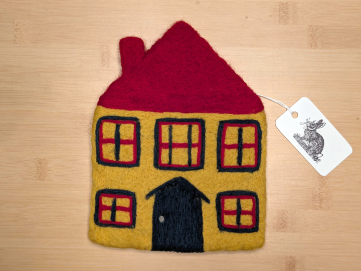A felted yellow house with a red roof, green and red trim around the windows, and a green door.